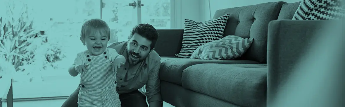 A father playing with his young child on the floor next to a sofa.